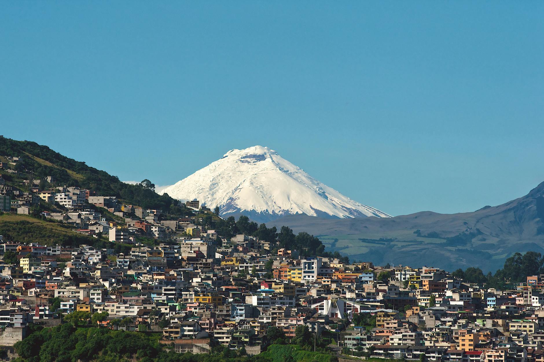 Explore Quito with the majestic backdrop of Cotopaxi Volcano under a clear blue sky.