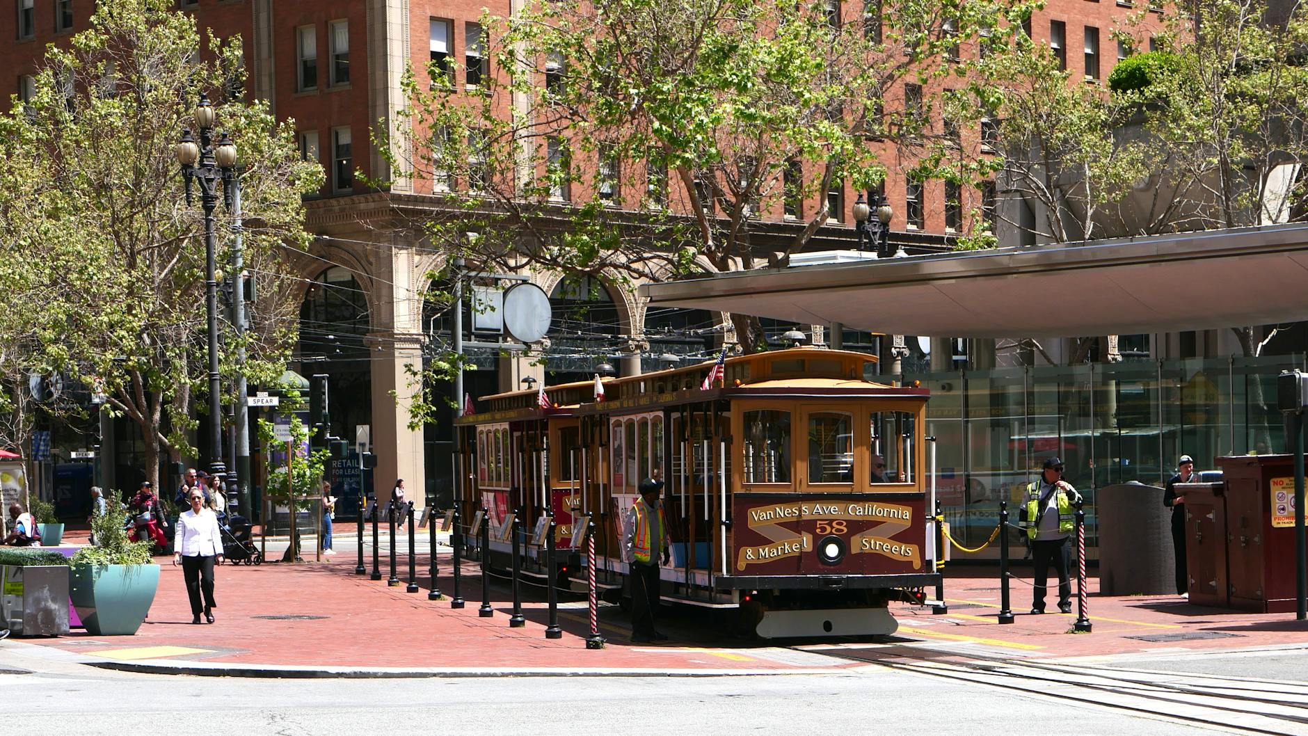 A classic San Francisco cable car stops on a sunny day with buildings in the background.