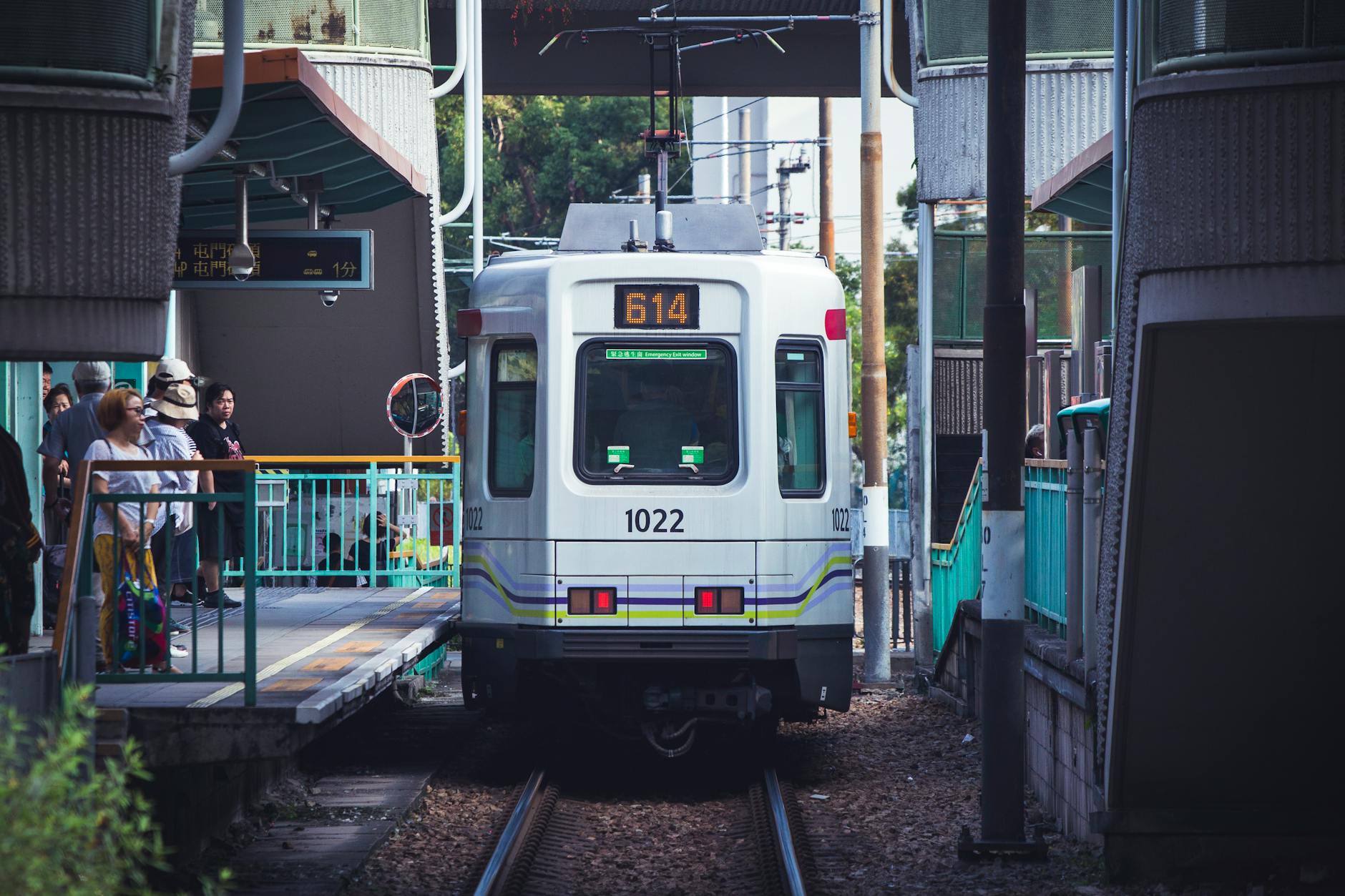 A Hong Kong tram approaches a busy station filled with people outdoors during daytime.