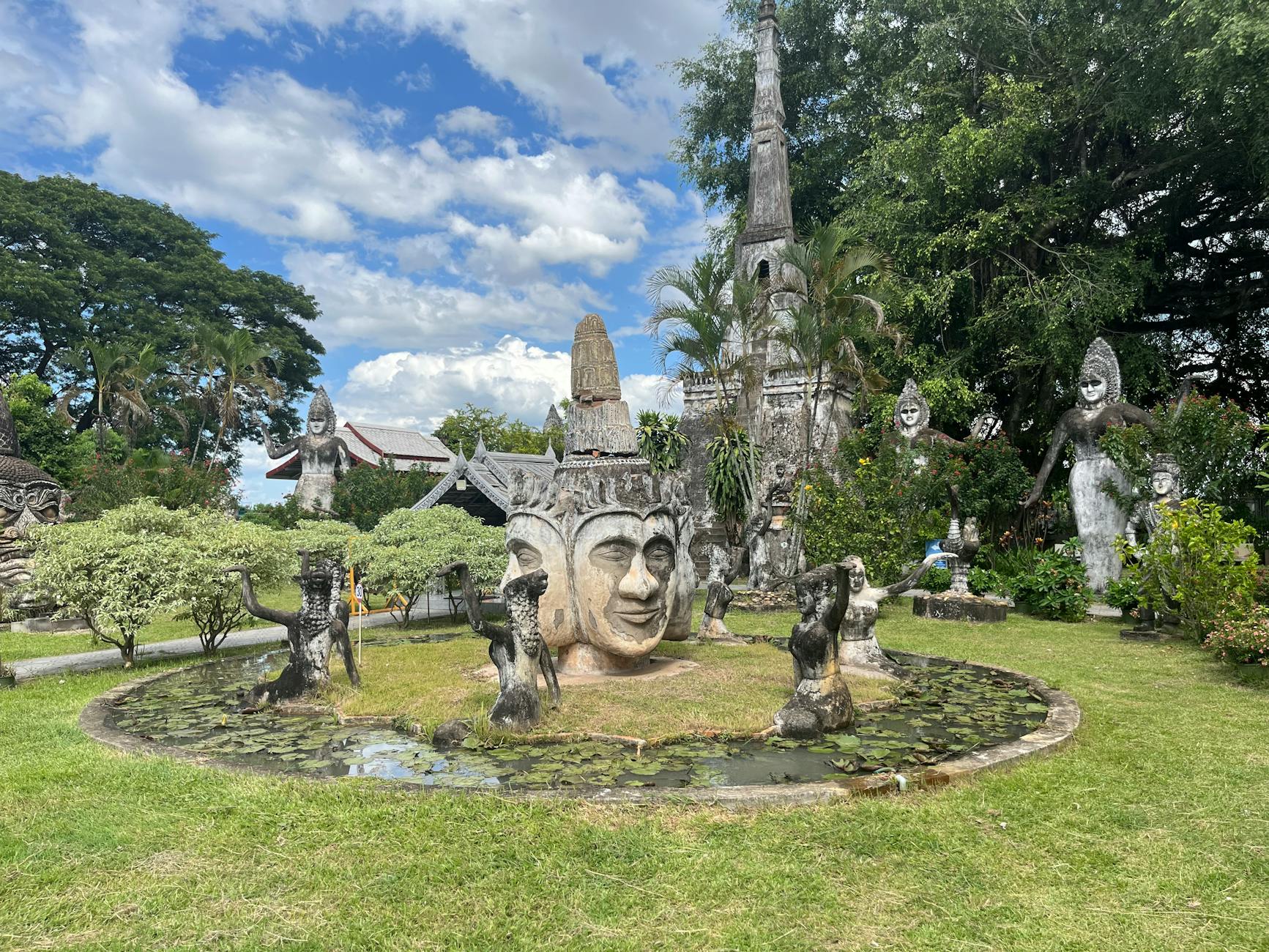 Sculpture park featuring Buddha statues amidst greenery and under a bright blue sky.
