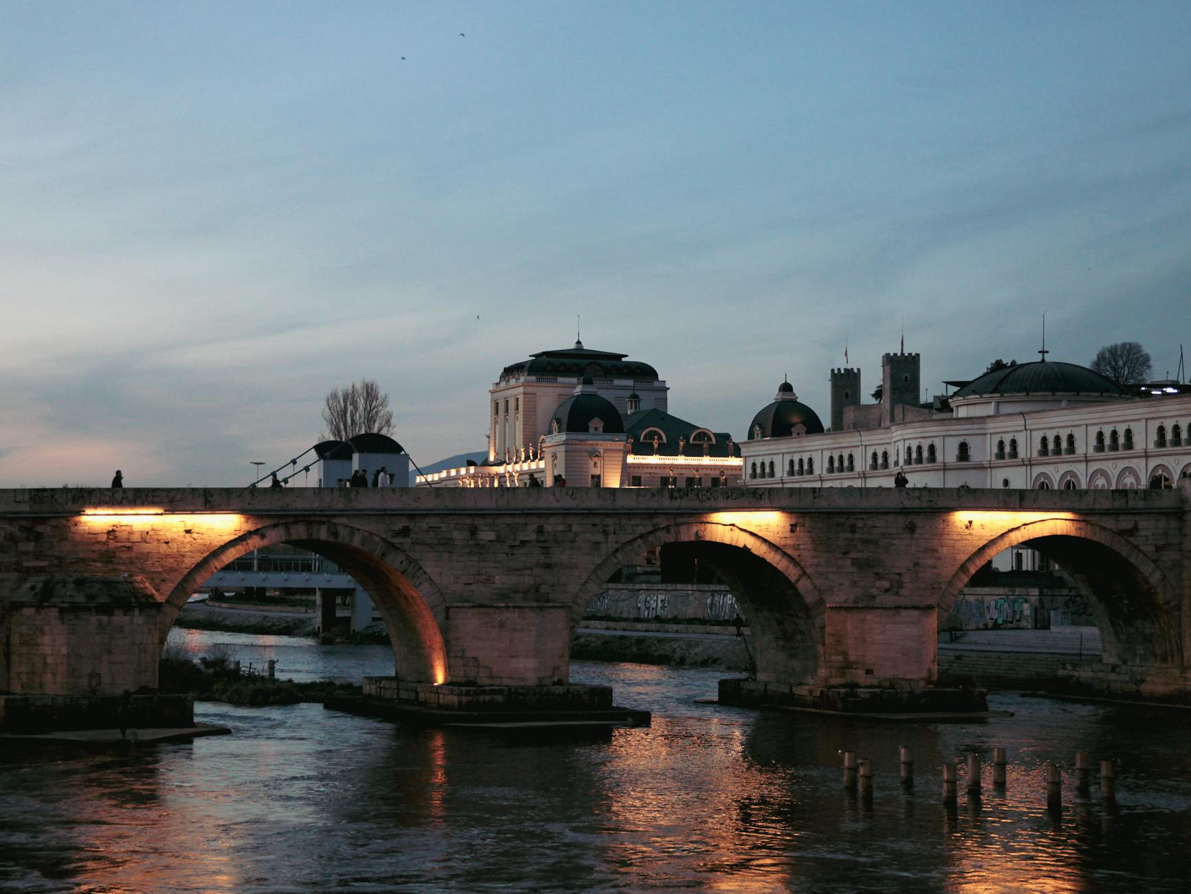 Evening shot of Stone Bridge over Vardar River in Skopje, illuminated by lights.