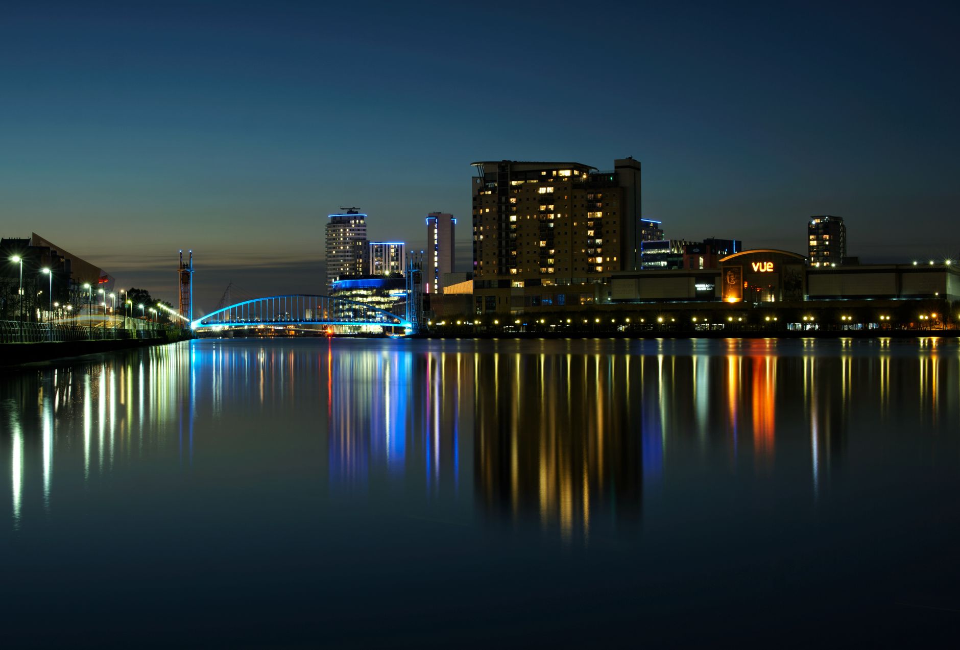 Nightscape of Salford Quays with illuminated buildings and water reflections in Manchester, England.
