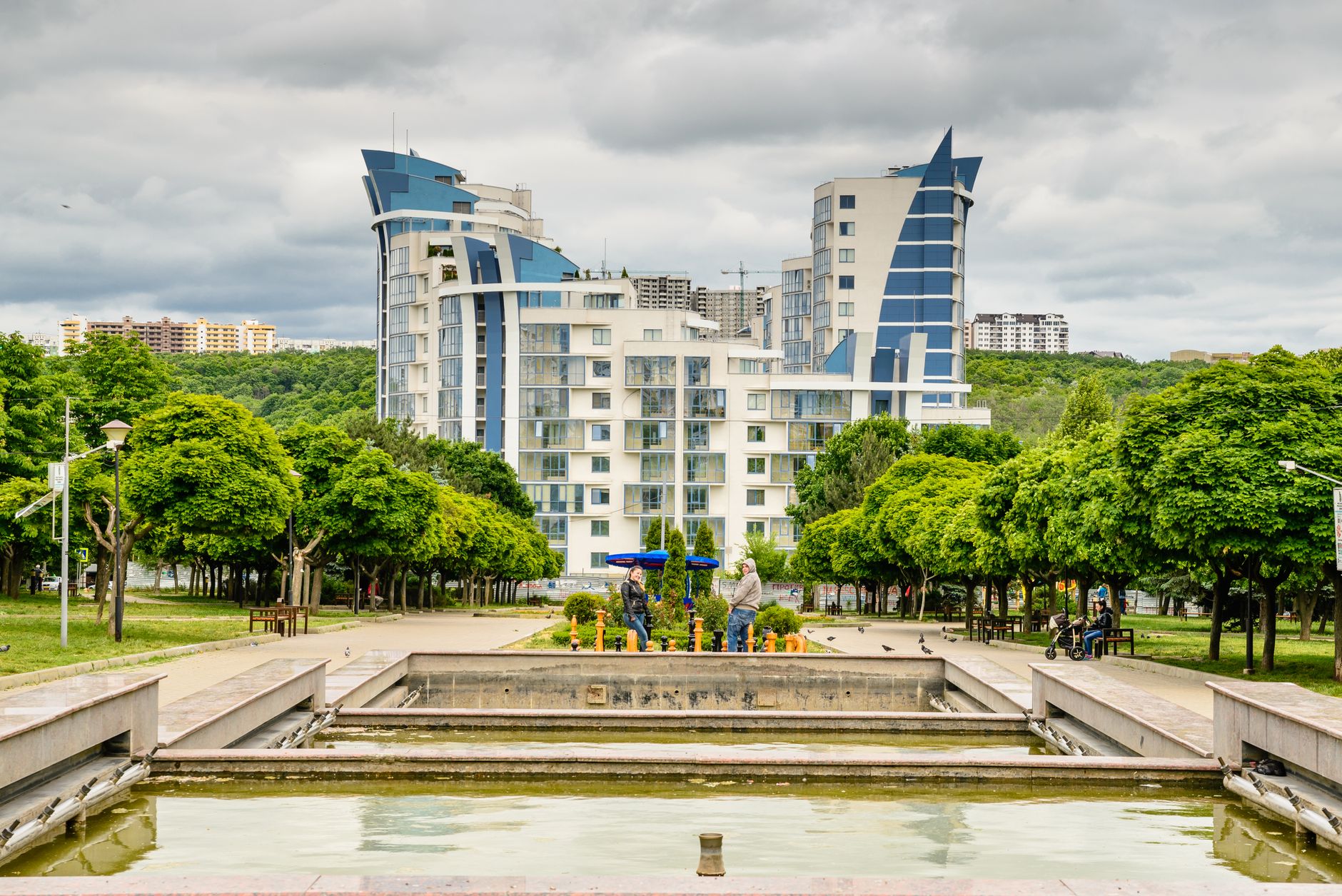 Explore modern buildings and lush greenery in a vibrant Chișinău park setting with a serene pond view.
