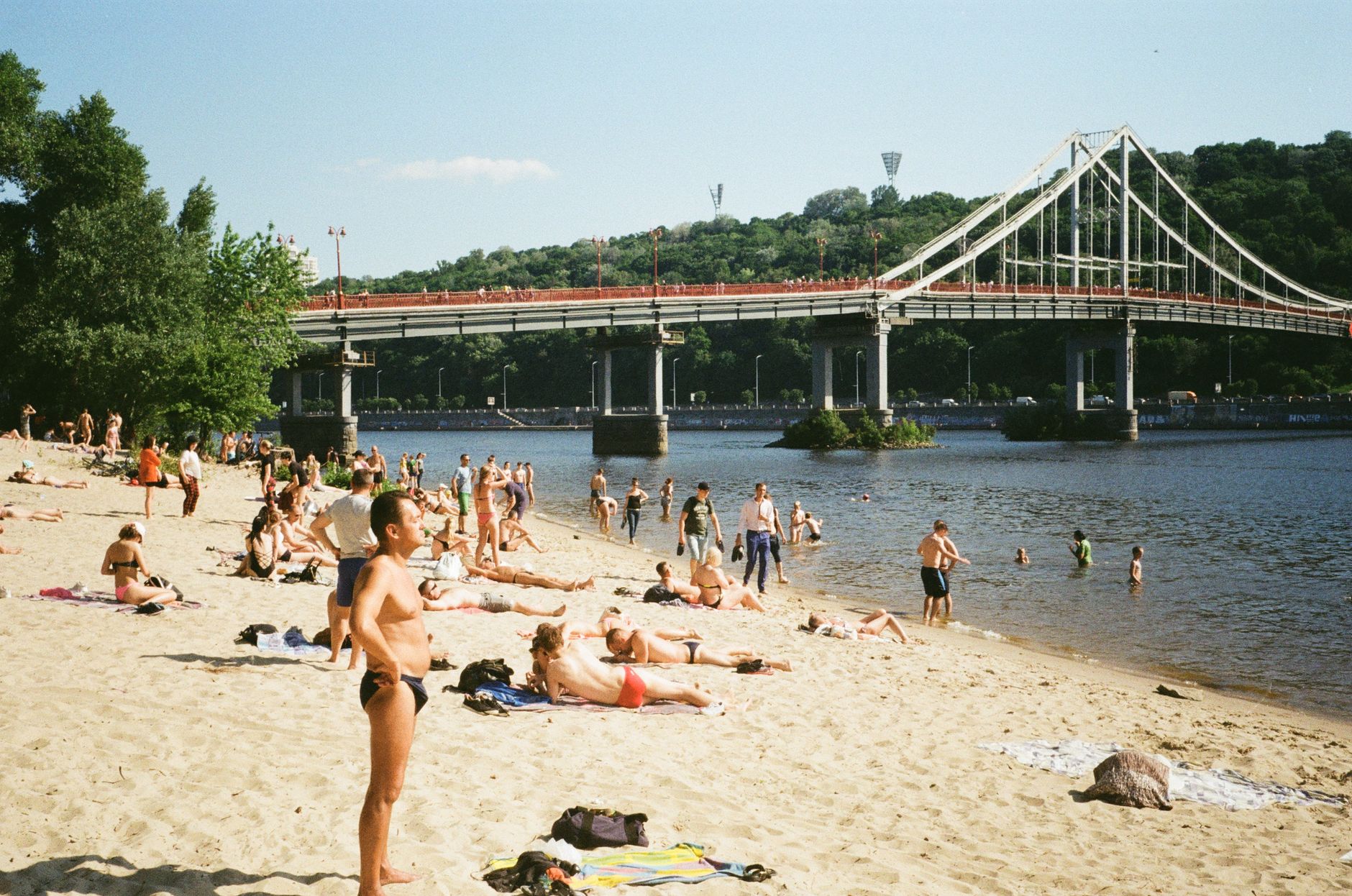 People enjoy a sunny day on the sandy beach by the Dnieper River in Kyiv, near Park Bridge.