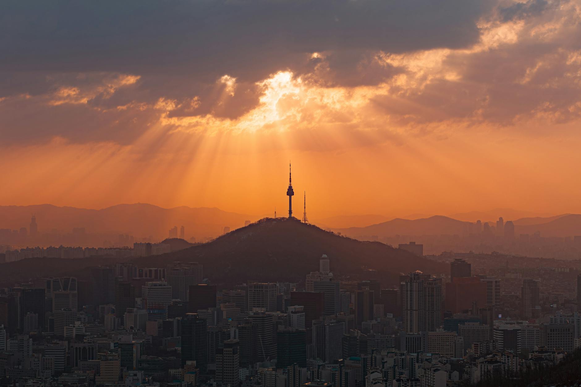 A breathtaking view of Seoul's skyline at sunset, featuring the iconic Namsan Tower under dramatic sunrays.