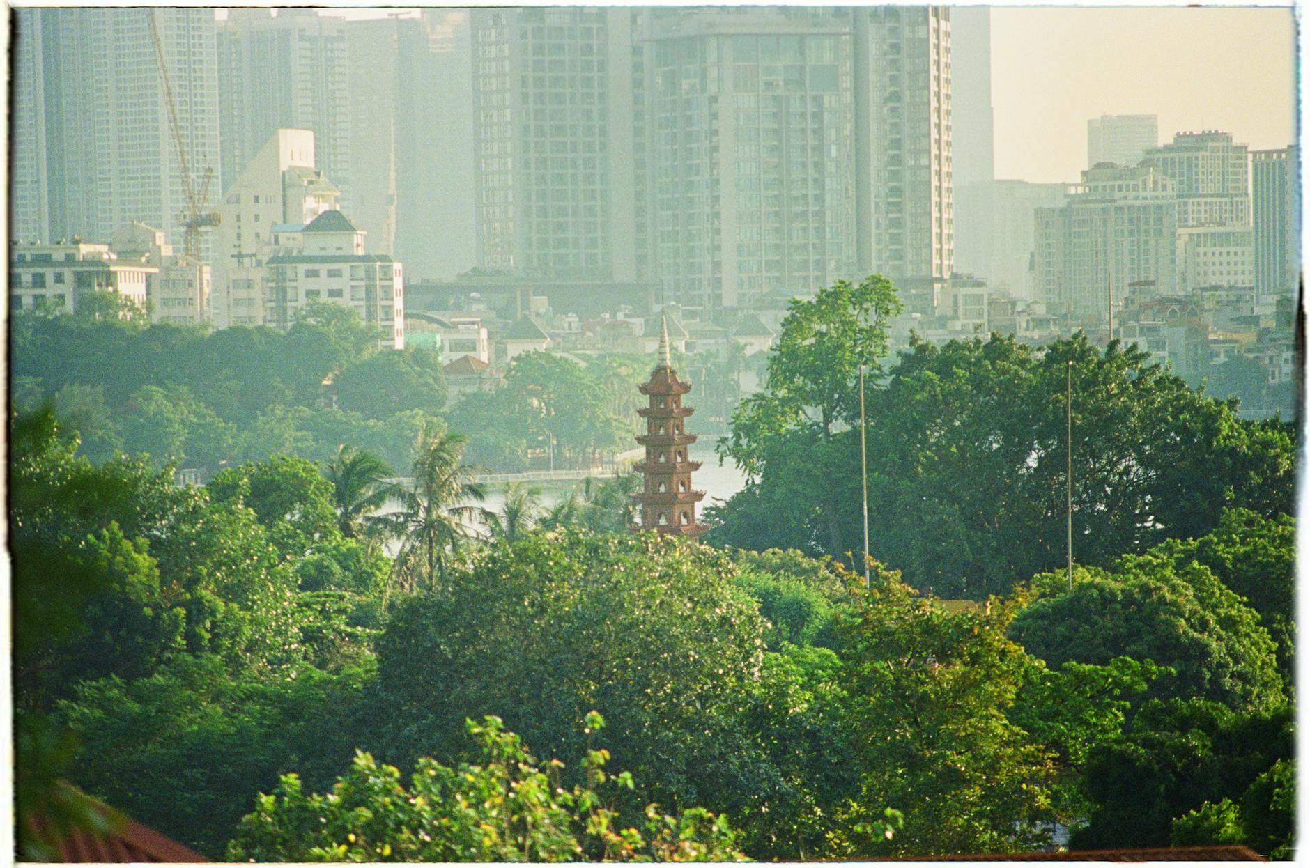 View of the Trấn Quốc Pagoda amidst trees and modern cityscape in Hà Nội, Vietnam.