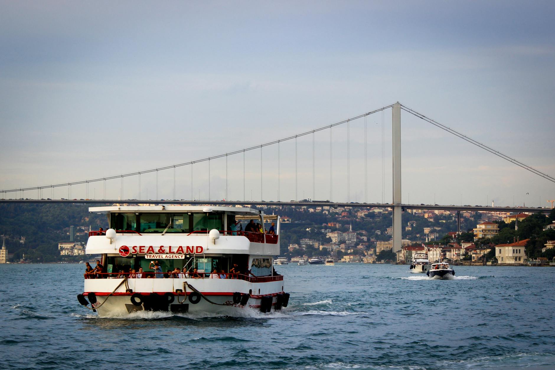 A ferry boat cruising under the iconic Bosphorus Bridge in Istanbul, Turkey.