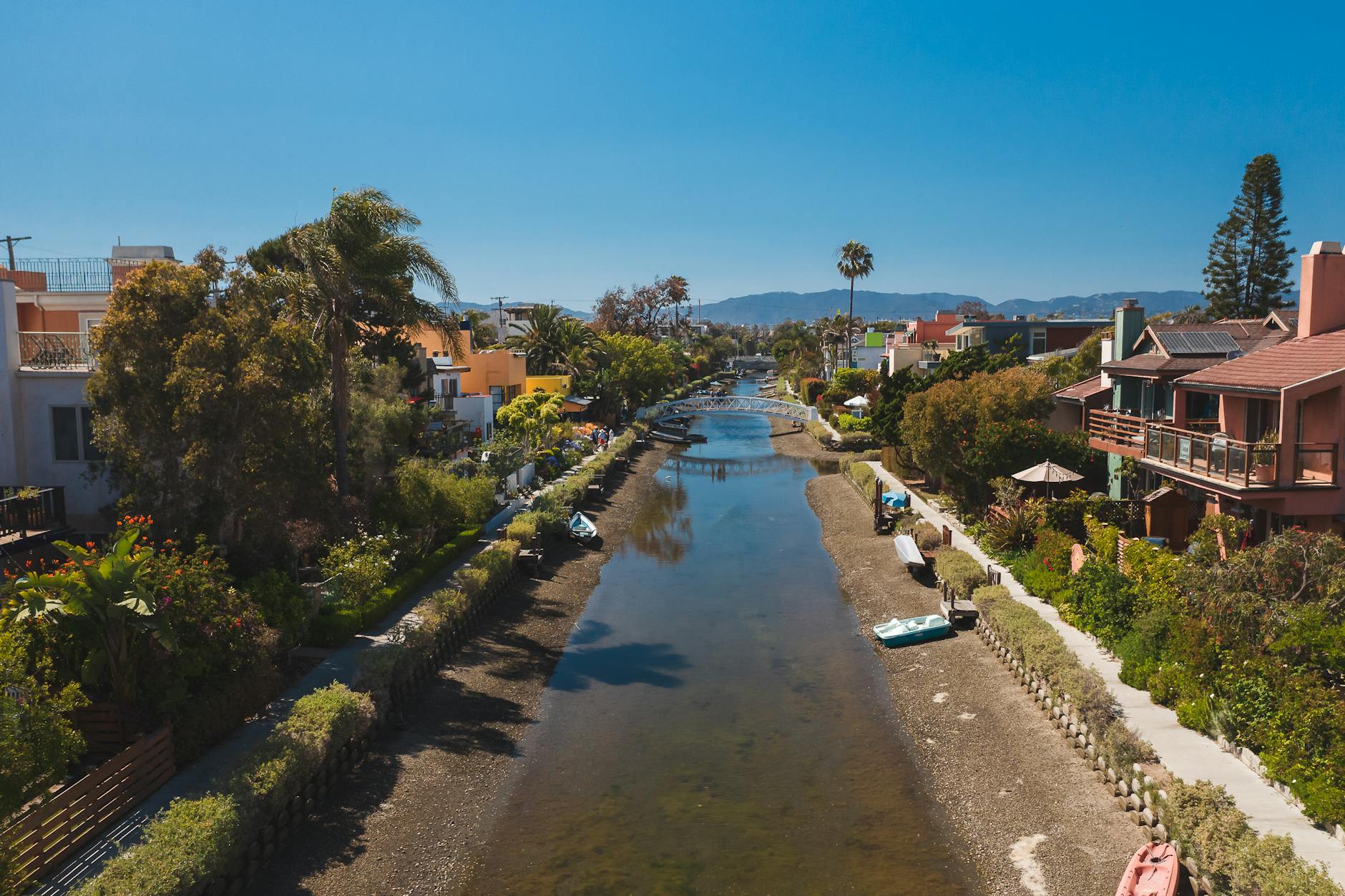 Picturesque canal with boats and houses under a clear summer sky, surrounded by lush vegetation.