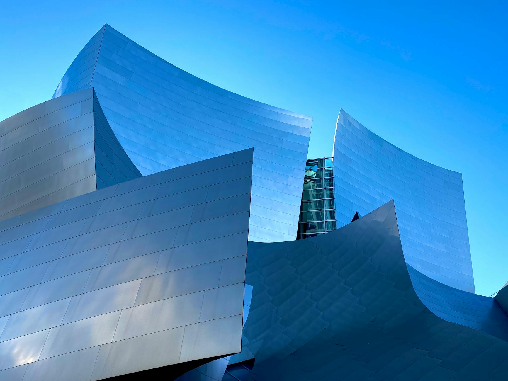 Striking low-angle view of the modern Walt Disney Concert Hall in Los Angeles against a blue sky.
