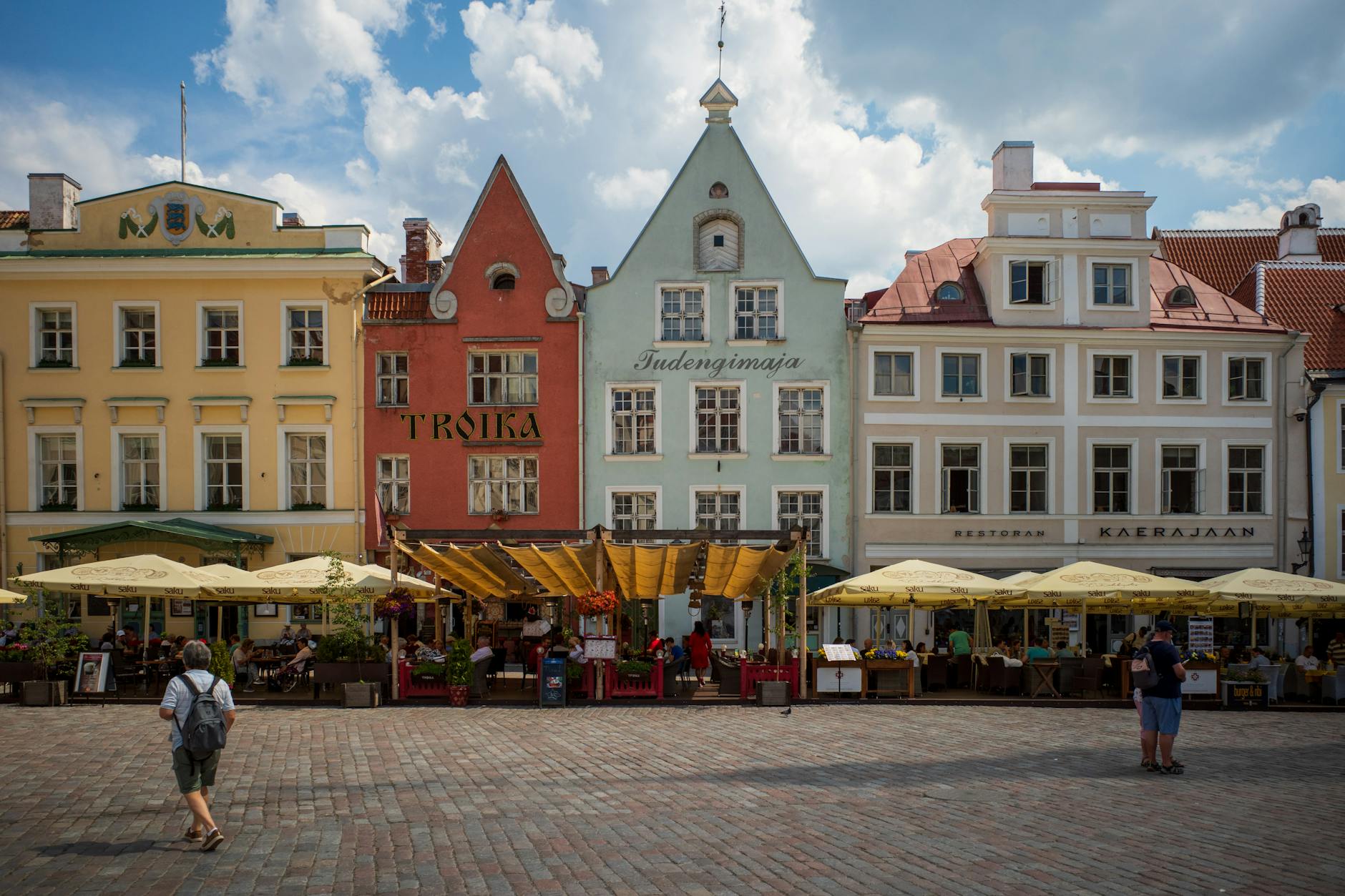 Vibrant city square in Tallinn with colorful historic buildings and bustling outdoor cafes.