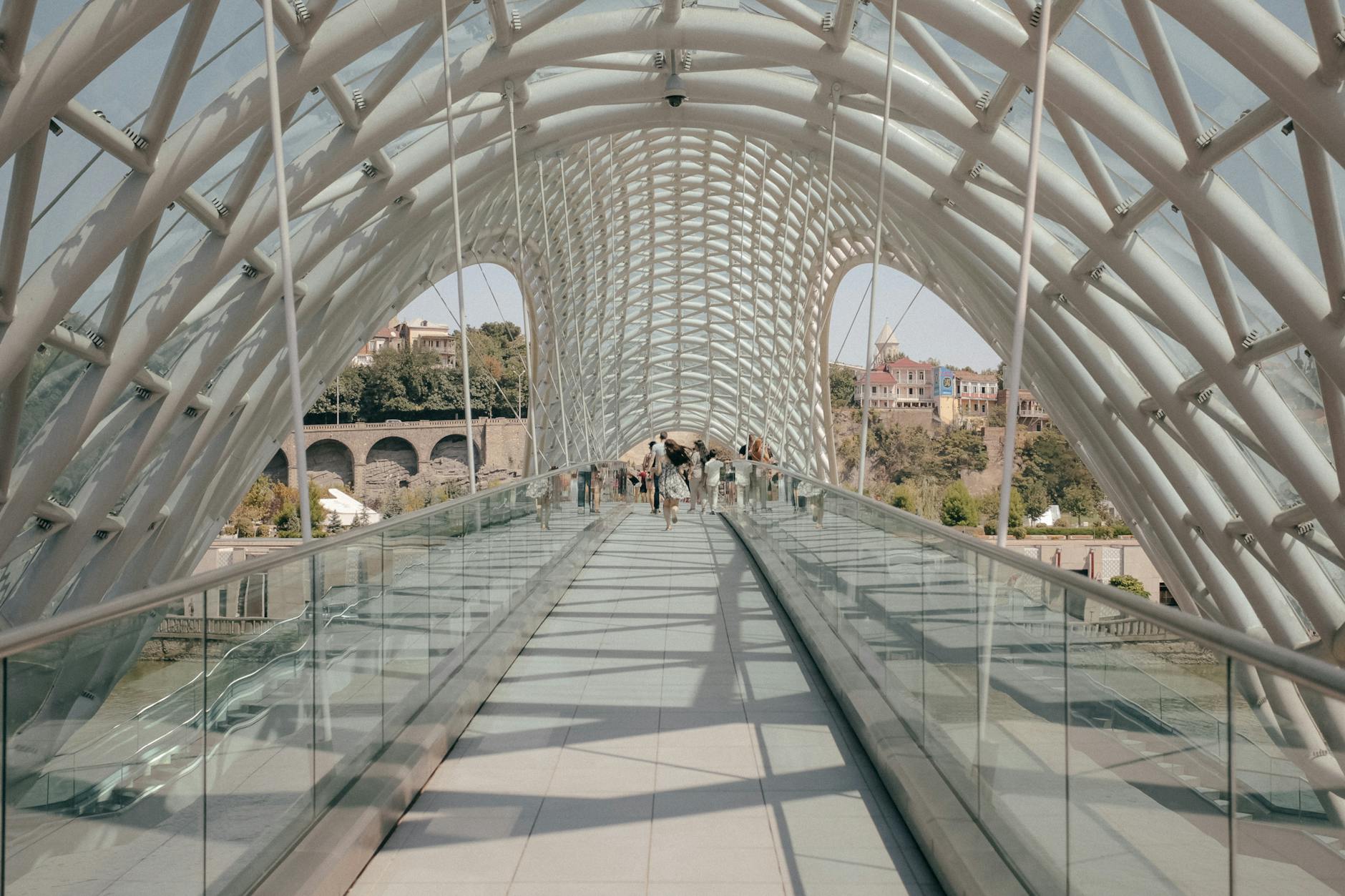 View of Tbilisi's iconic Peace Bridge with people walking under its modern architectural canopy.
