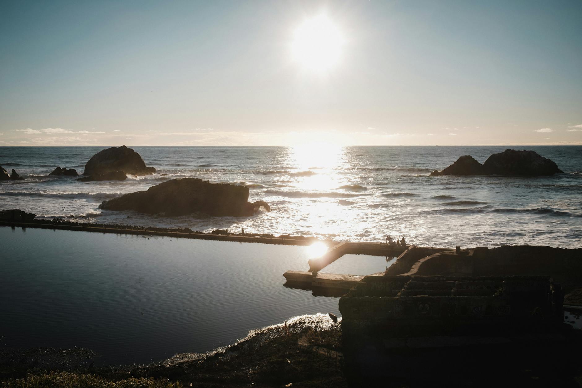 A breathtaking view of the sunset over the historic Sutro Baths and Ocean Beach with waves crashing against rocks.