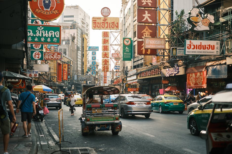 Bustling street scene in Bangkok's Chinatown with colorful signs and tuk-tuks.