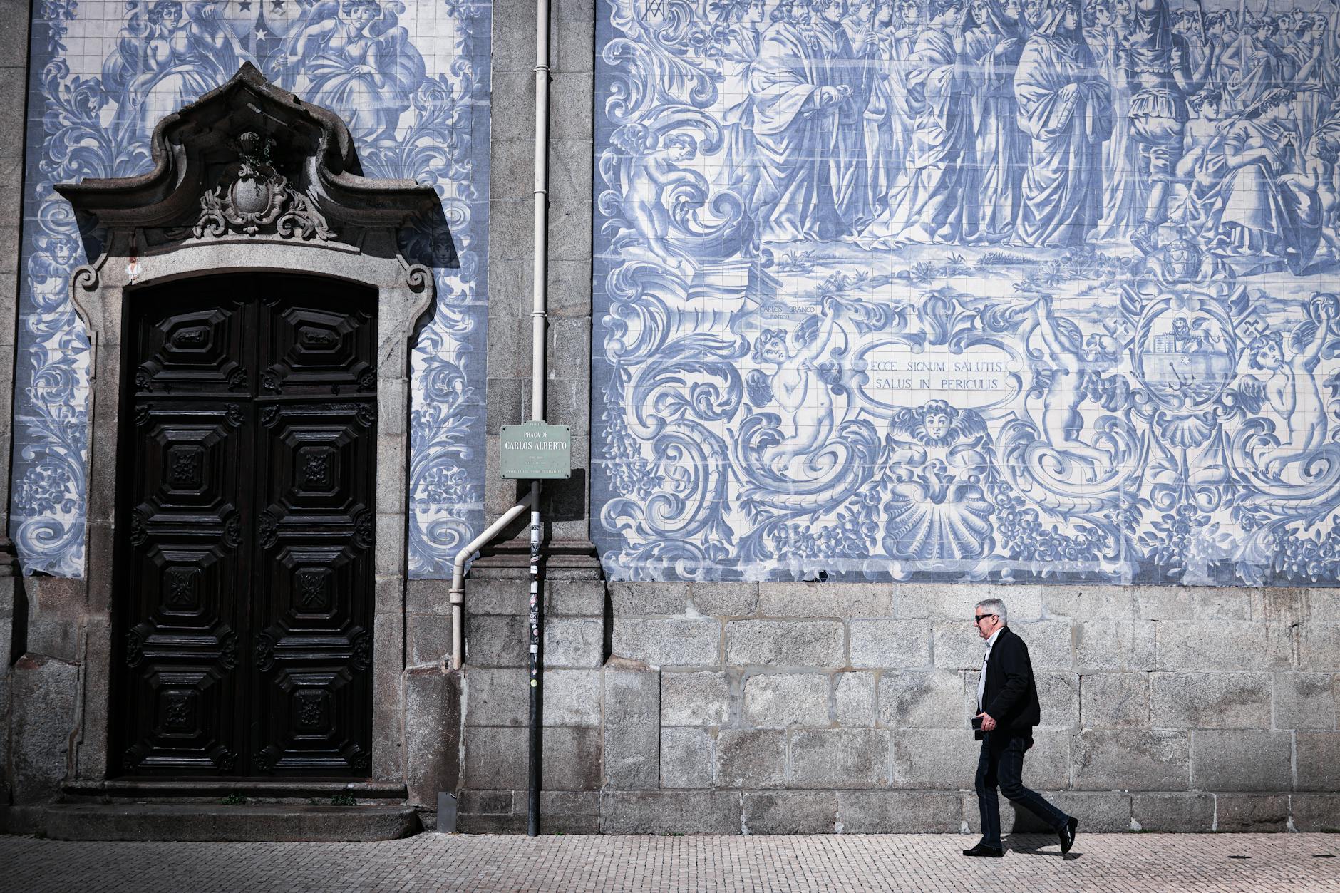 A man walks by a traditional azulejo wall in Porto, capturing the essence of Portuguese art and culture.