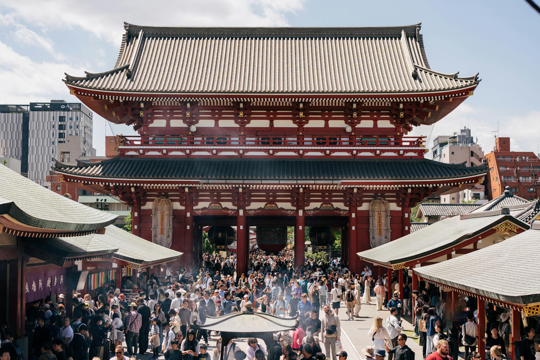 Vibrant scene at Senso-ji Temple in Tokyo with a large crowd on a sunny day, showcasing traditional architecture.