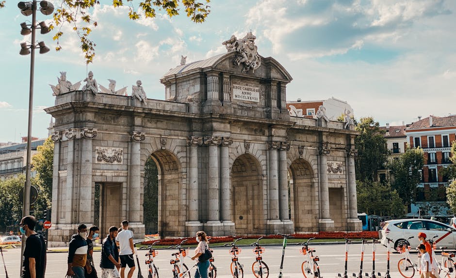 View of Puerta de Alcalá with pedestrians and scooters in vibrant Madrid.