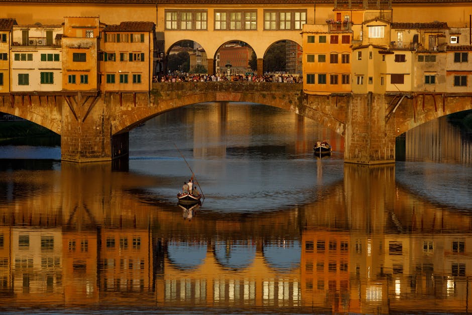 Ponte Vecchio reflecting in water under a golden sunset in Florence, Italy.