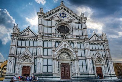 Beautiful facade of the Basilica di Santa Croce in Florence under dramatic clouds and sunlight.