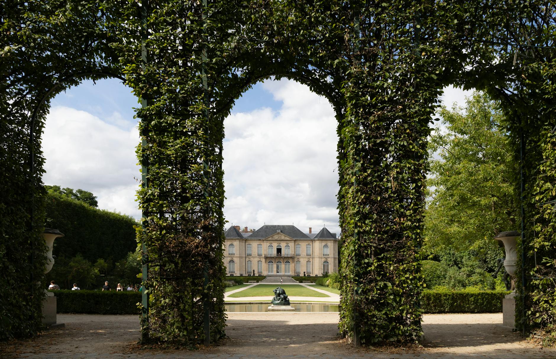 Serene view of a historic château in Paris through lush green archway in summer.