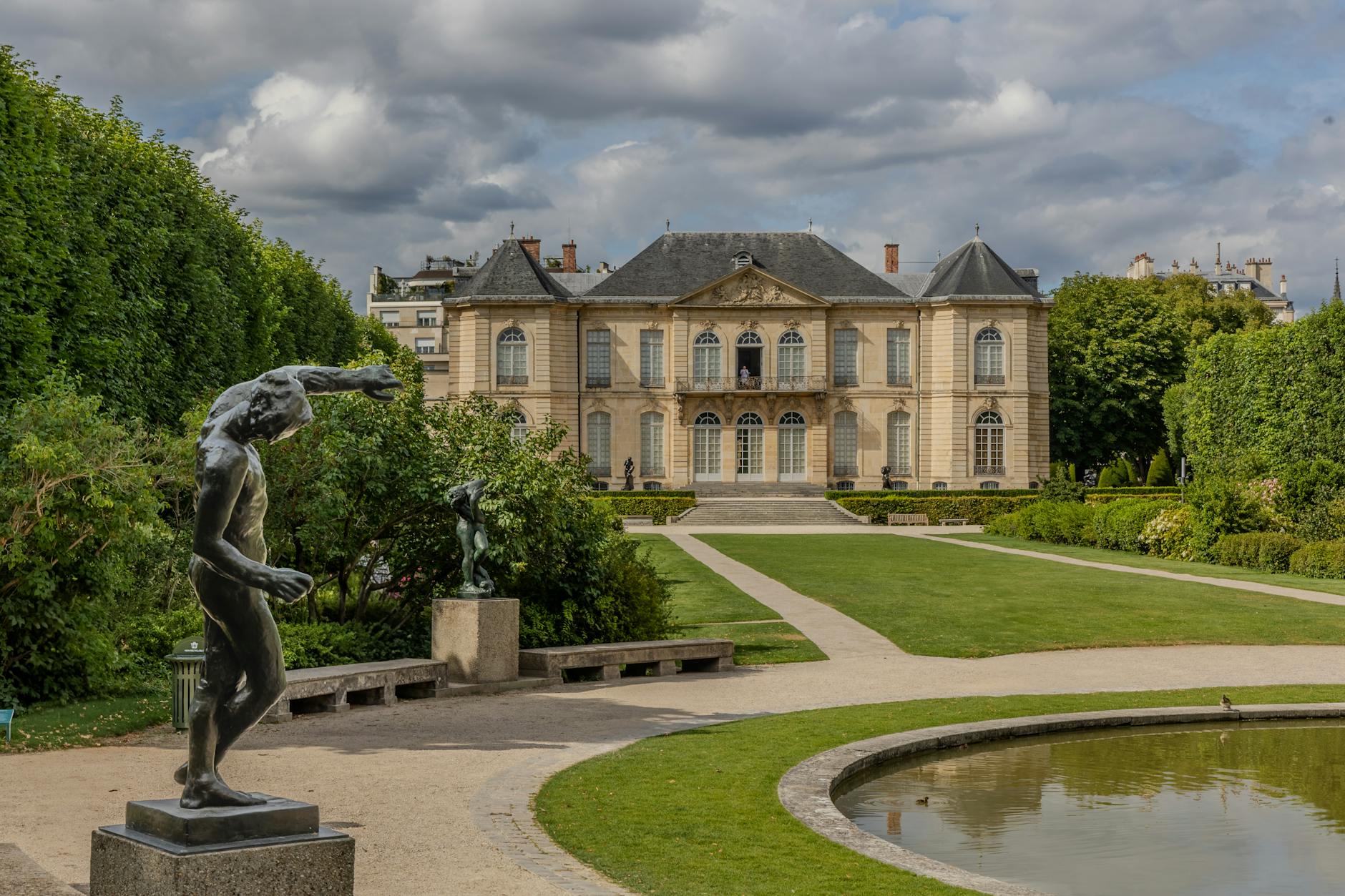 Tranquil garden view of historic mansion in Paris, featuring lush greenery and sculptures.