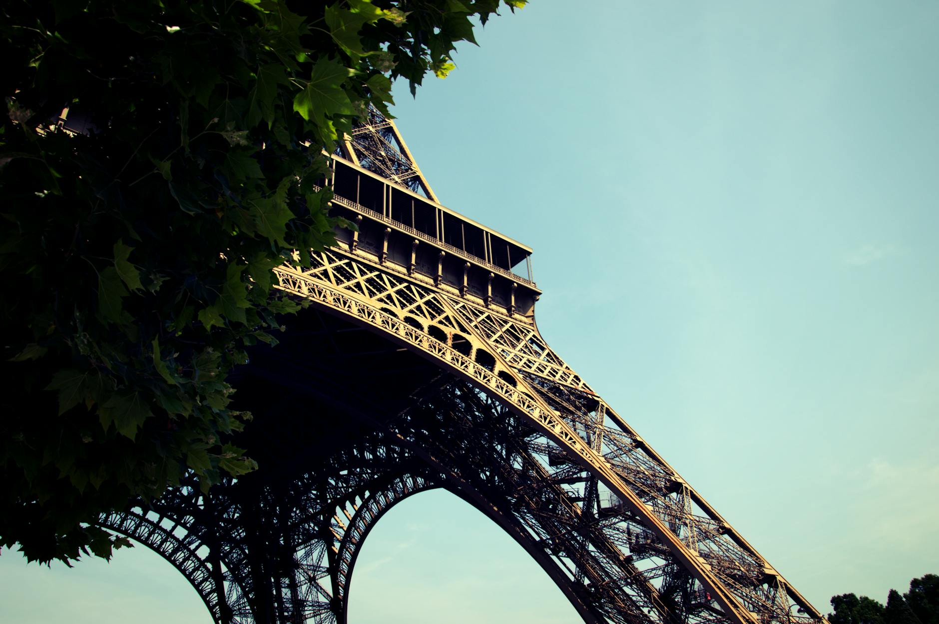 A low angle shot of the iconic Eiffel Tower in Paris with vivid blue sky and leafy trees.