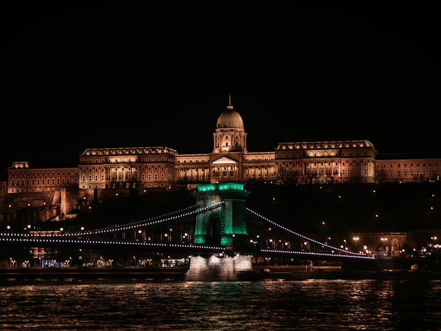 Illuminated view of Buda Castle and Széchenyi Chain Bridge over the Danube River in Budapest at night.