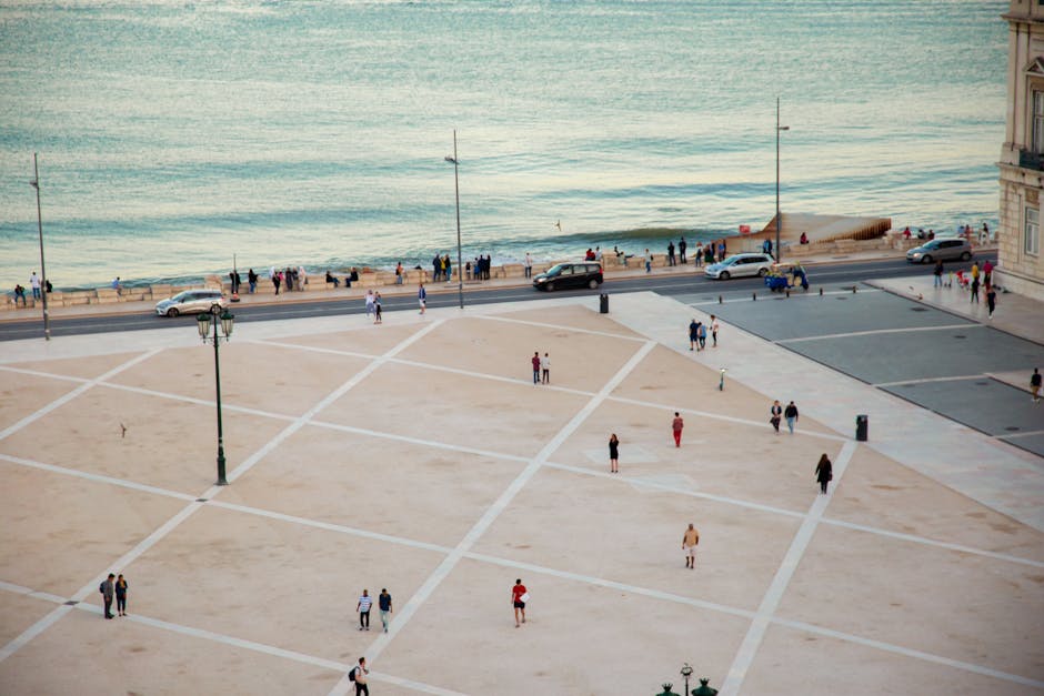Wide angle view of people strolling at Praça do Comércio by the waterfront in Lisbon.
