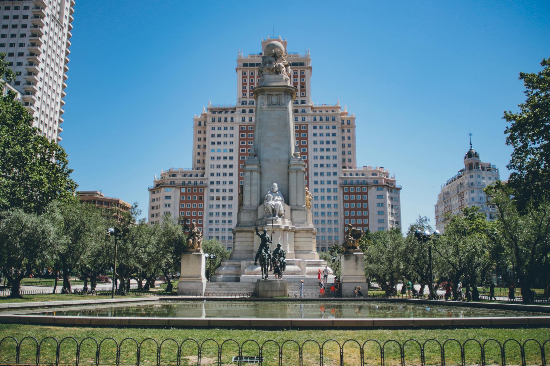 View of the monumental statue in Plaza de España, Madrid, surrounded by modern buildings and greenery.