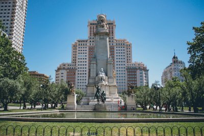 View of the monumental statue in Plaza de España, Madrid, surrounded by modern buildings and greenery.