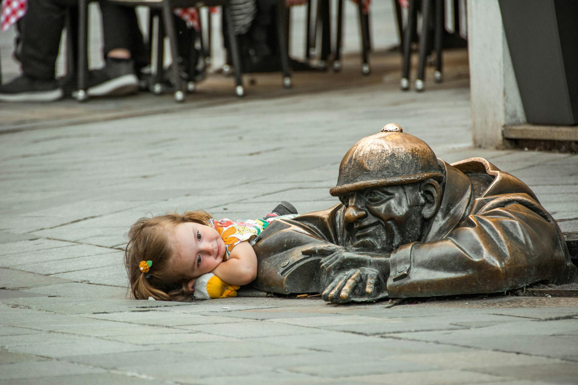 A child lies beside the iconic Cumil statue on a street in Bratislava, creating a charming scene.