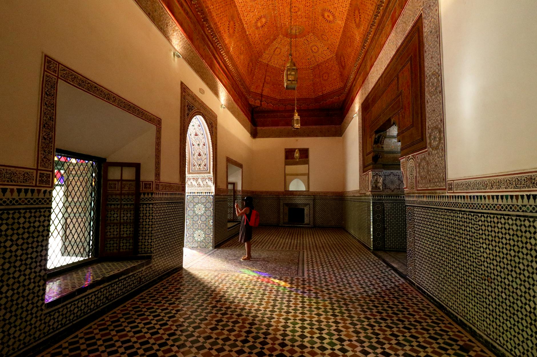 A person in a traditional Moroccan hall with ornate tilework and stained glass at Bahia Palace, Marrakech.
